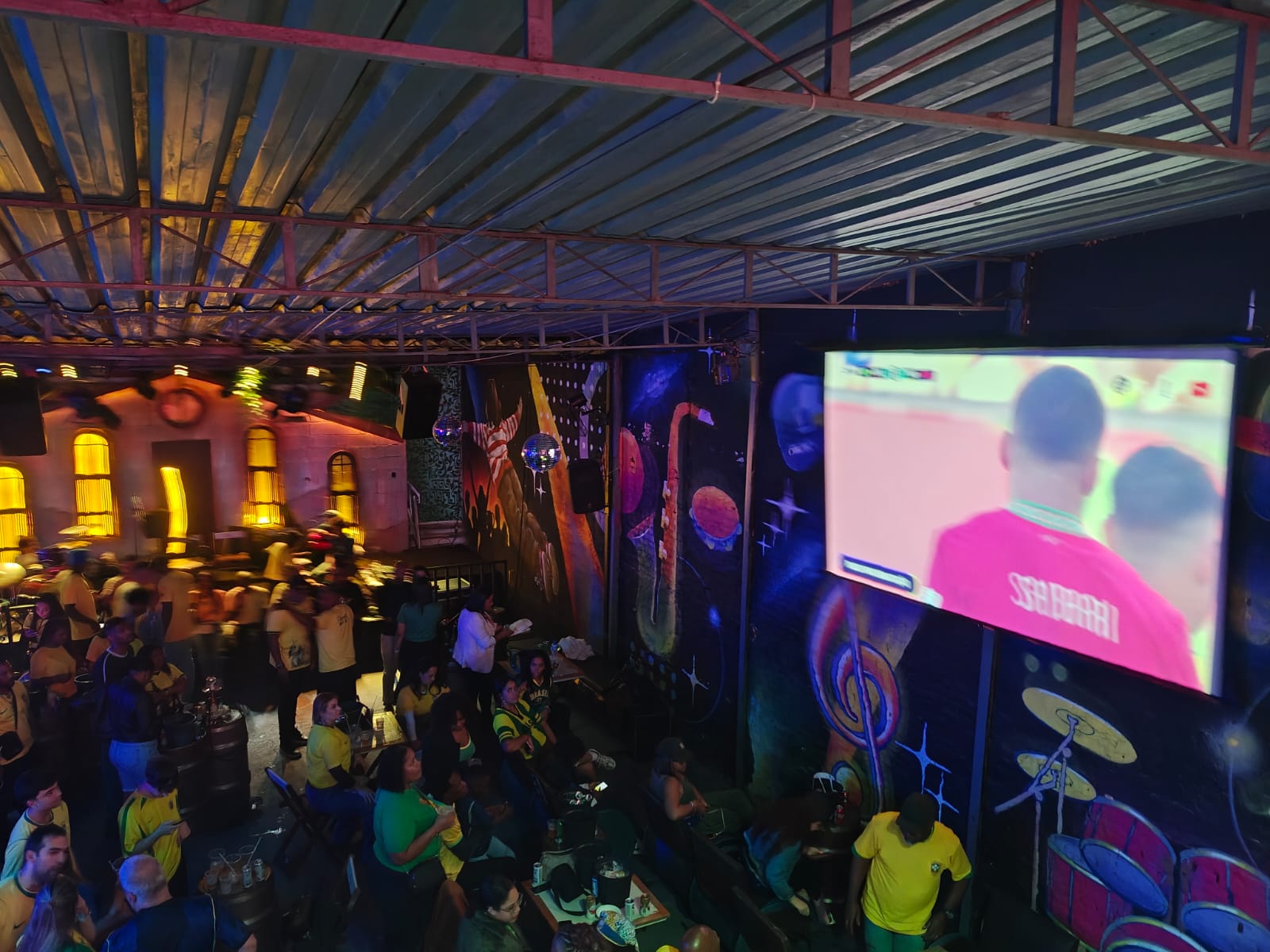 Vista panorâmica da Villa do Som lotada em noite de Copa do Mundo com telão gigante e mural grafitado ao fundo